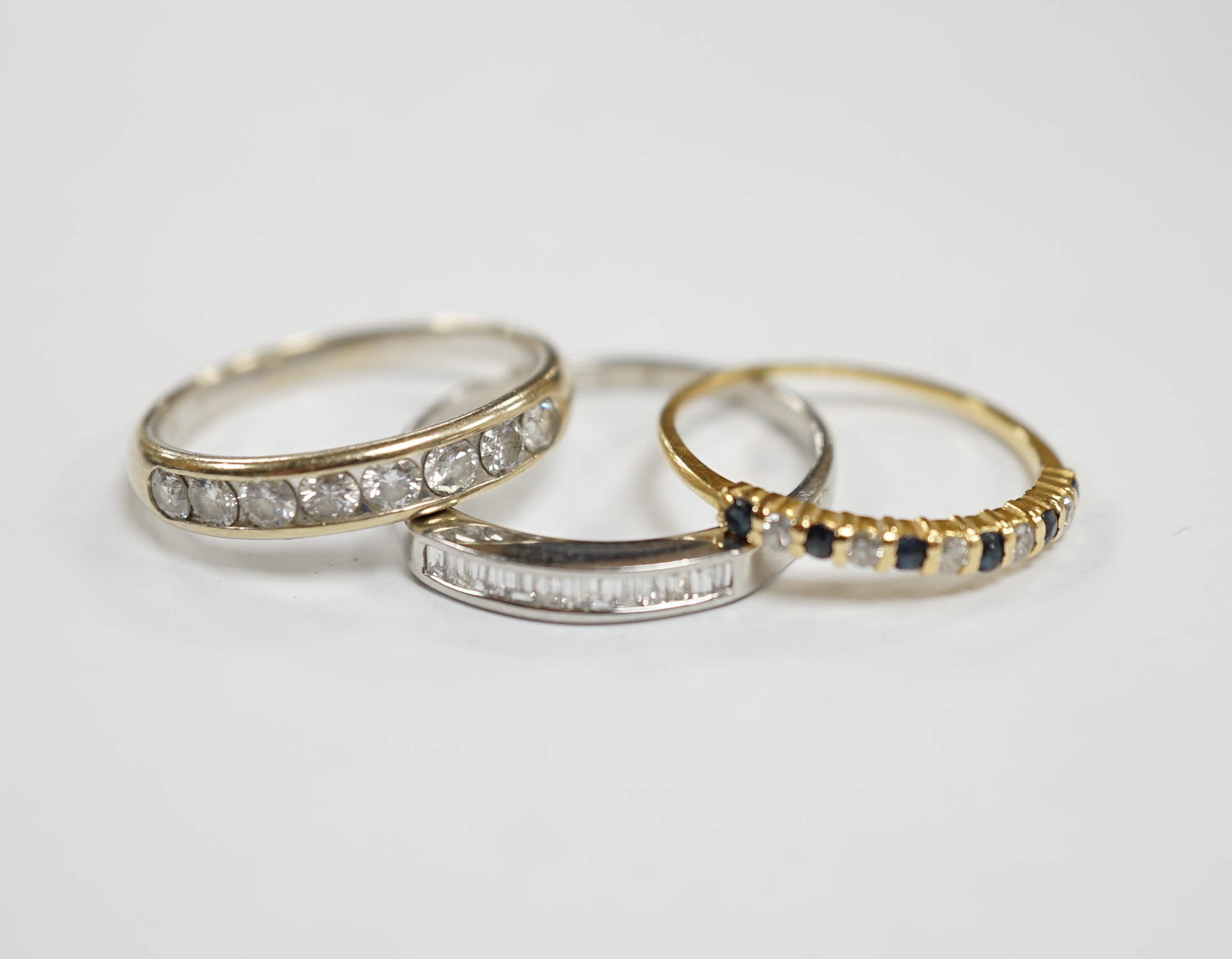 A white metal (stamped 950) and thirteen stone channel set baguette cut diamond ring, size O, together with two other unmarked gem set rings including diamond half eternity ring.